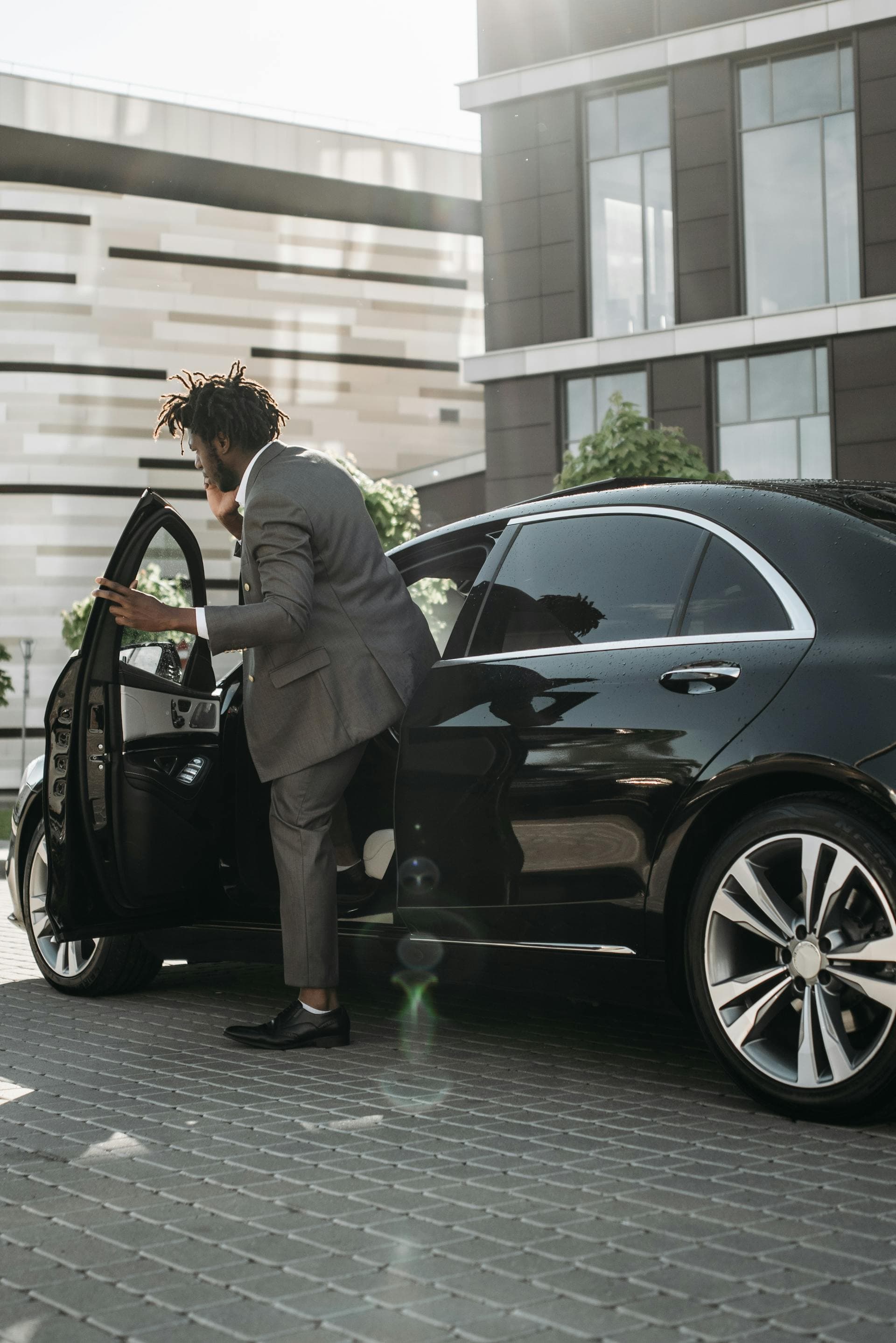 Businessman exiting black luxury sedan at modern building, Adelaide airport chauffeur vs shuttle comparison