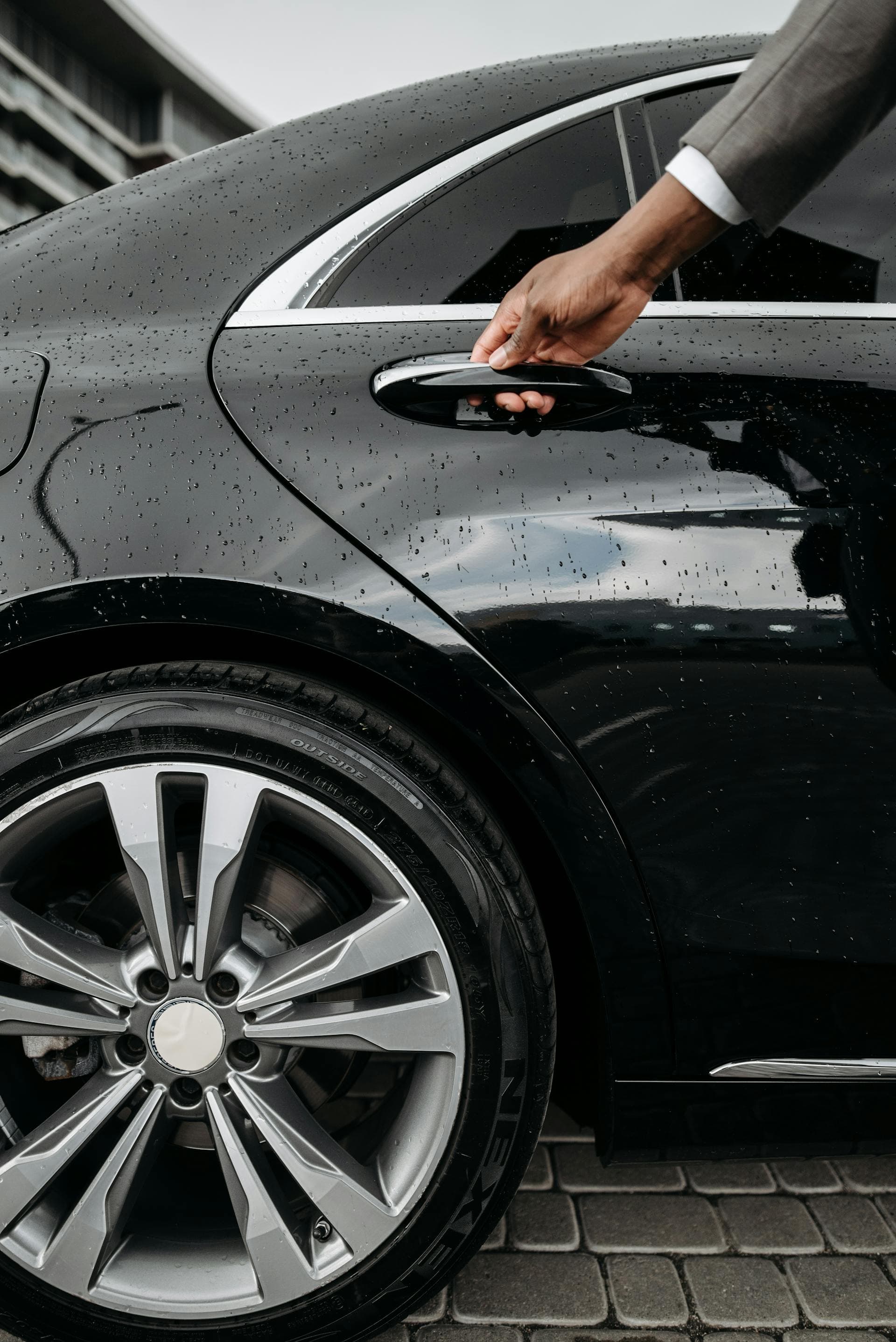 Hand opening rear door of black luxury sedan, Adelaide chauffeur hourly rates explained
