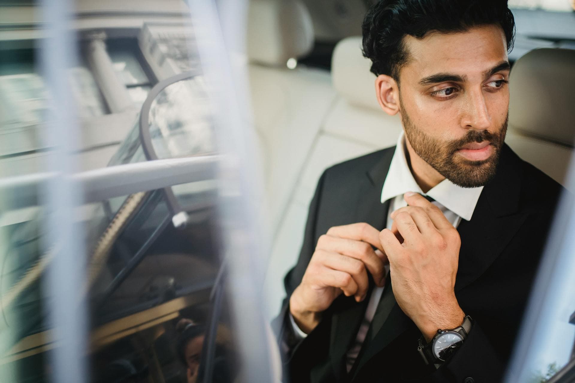 Man in black suit adjusting tie inside vehicle, Adelaide chauffeur tipping etiquette guide