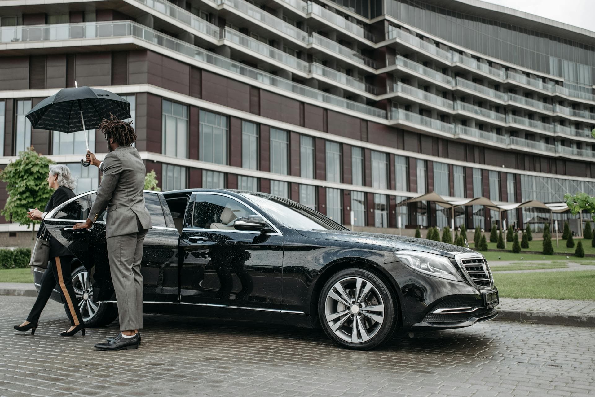 Chauffeur in black suit with umbrella beside luxury sedan, Adelaide chauffeur pricing